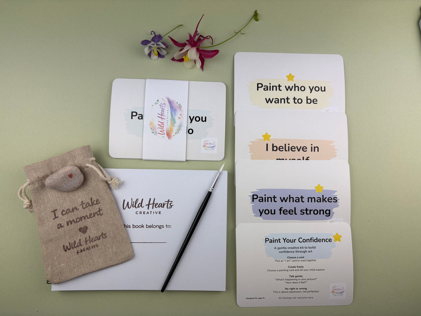 Flat lay of the paint your confidence creative support kit for children, featuring prompt cards, comfort stones, creative resources and comfort items designed to support emotional wellbeing.