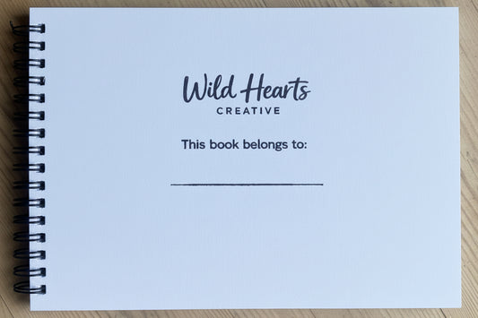 Notebook with 'Wild Hearts Creative' branding on a wooden surface.  Hand stamped for important moments