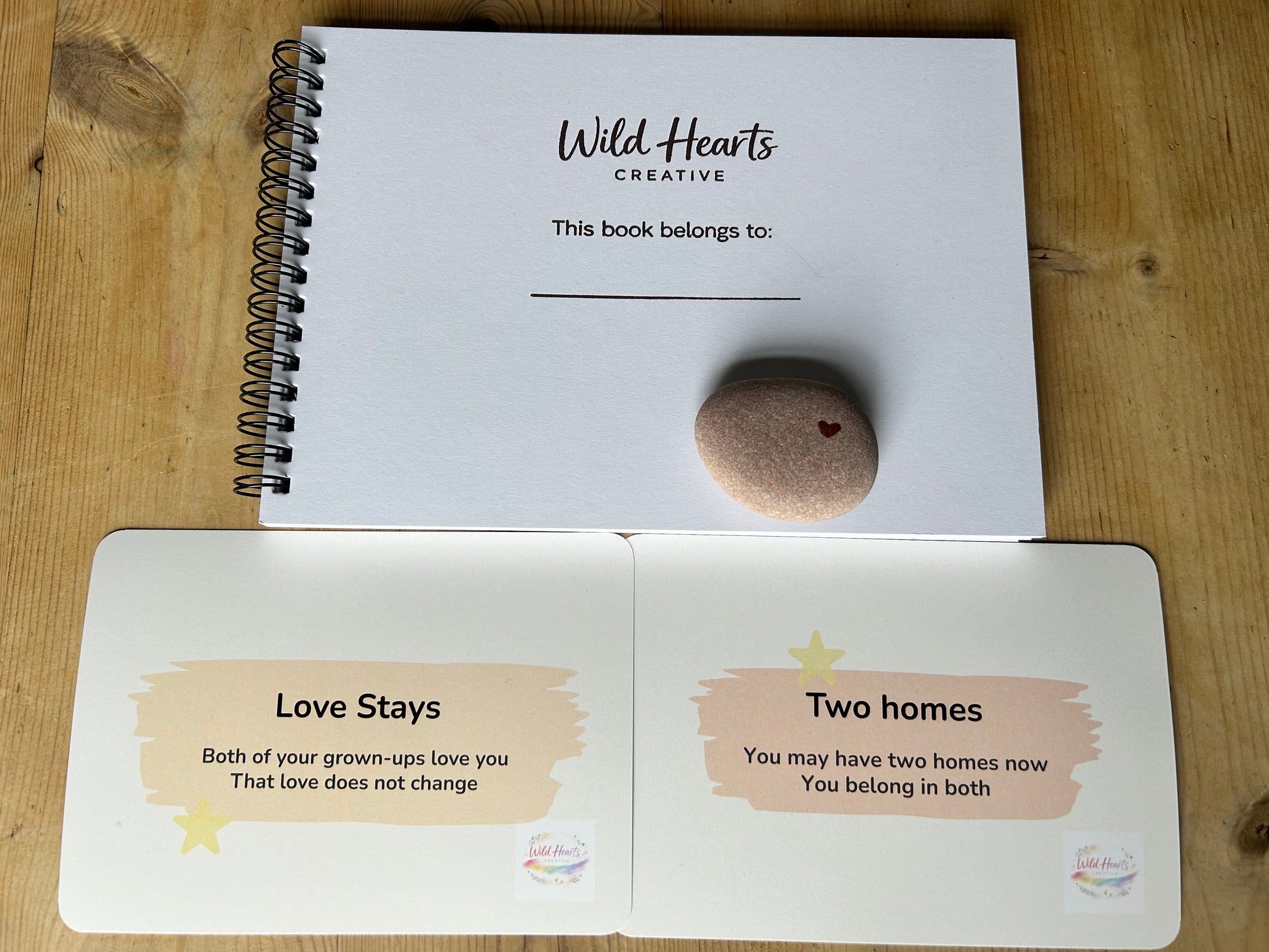 Children's personalised art sketchbook, on a wooden surface, featuring 'Wild Hearts Creative' branded Two Homes, One Me cards, with grounding stone.