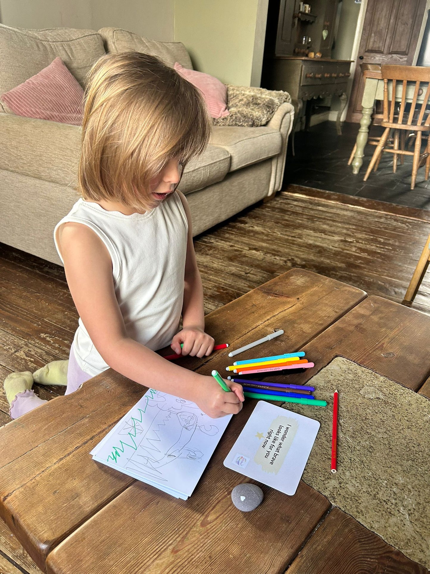 Child creatively playing at a wooden table with crayons and paper in a home setting