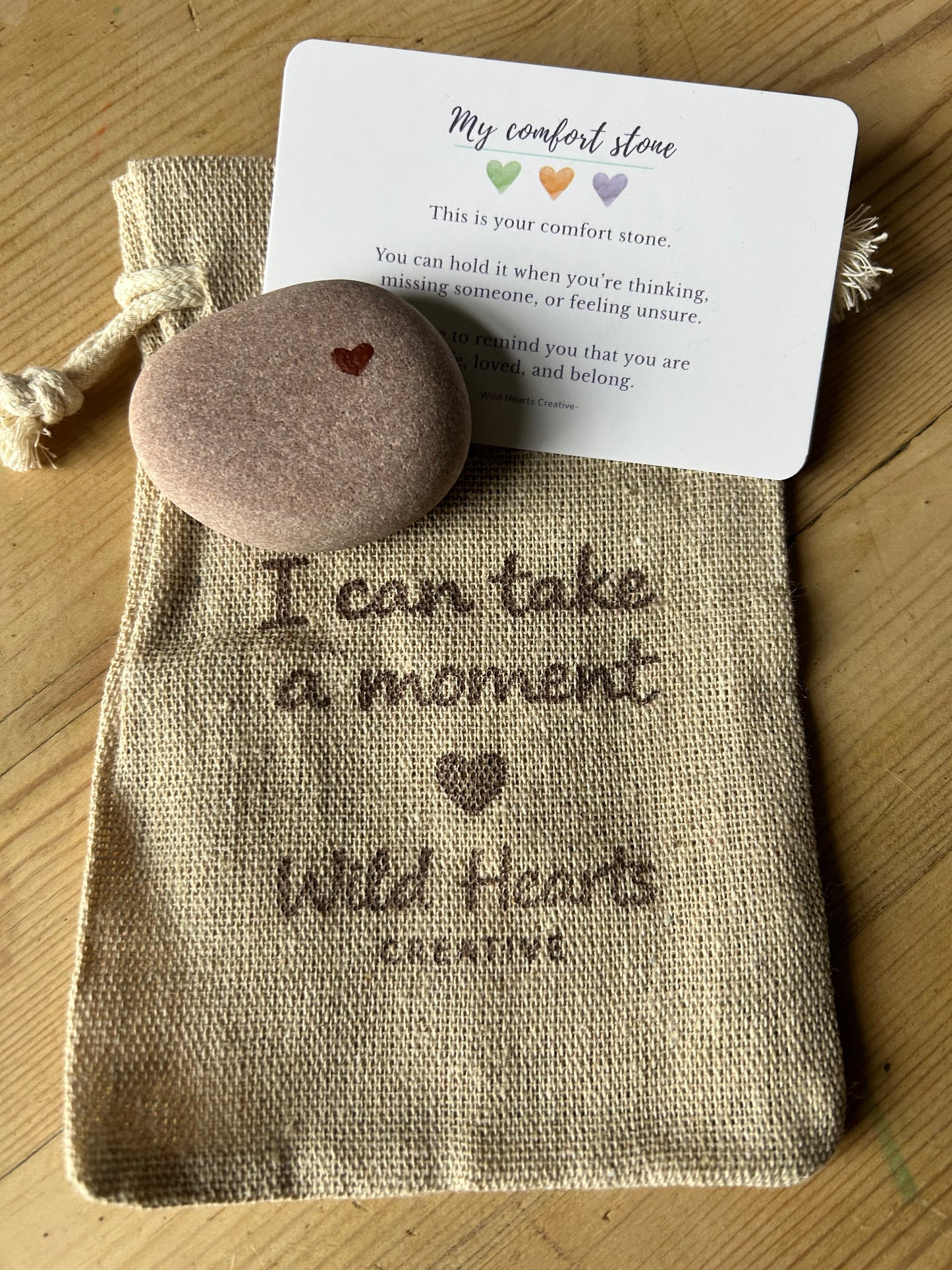 Decorative child's comfort stone with heart design in a drawstring bag with text, on a wooden surface.