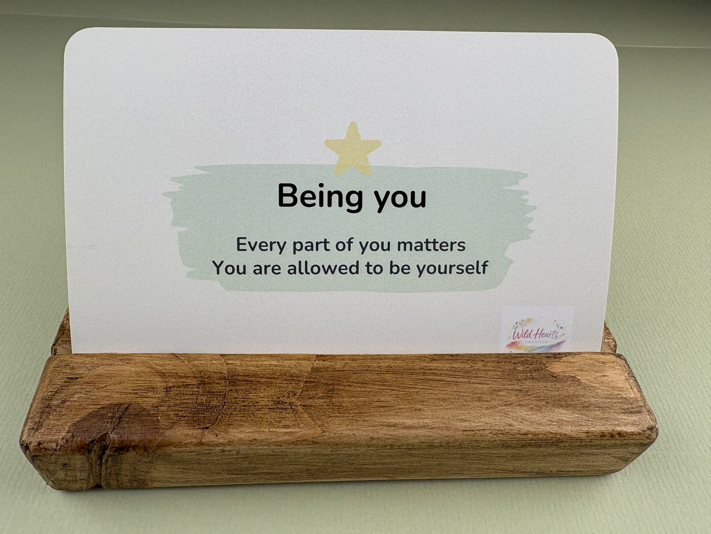 Motivational card with text 'Being you, every part of you matters, you are allowed to be yourself' on a wooden stand.