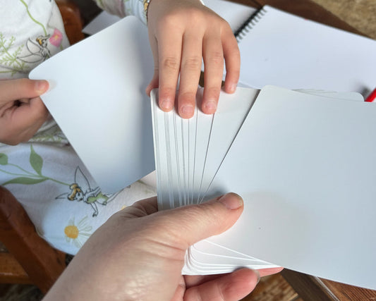 Two hands holding a stack of white cards on a wooden surface.