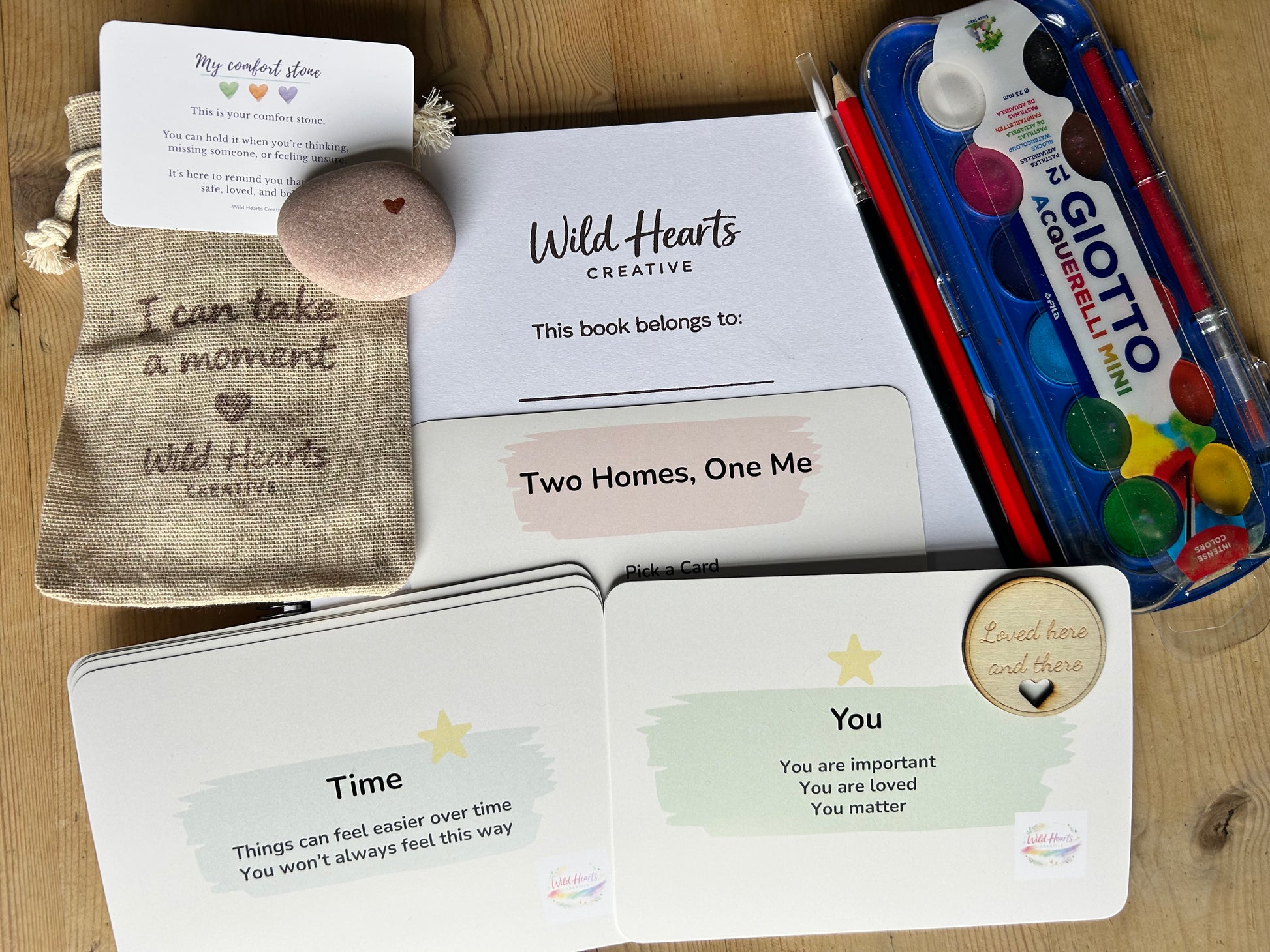 Children's book titled 'Two Homes, One Me' with a pen and watercolor set on a wooden surface. divorce and coparenting kit by Wild Hearts Creative