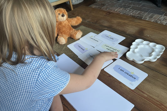 Child interacting with educational cards on a table with a teddy bear nearby.  Emotional Wellbeing support kit, more than words